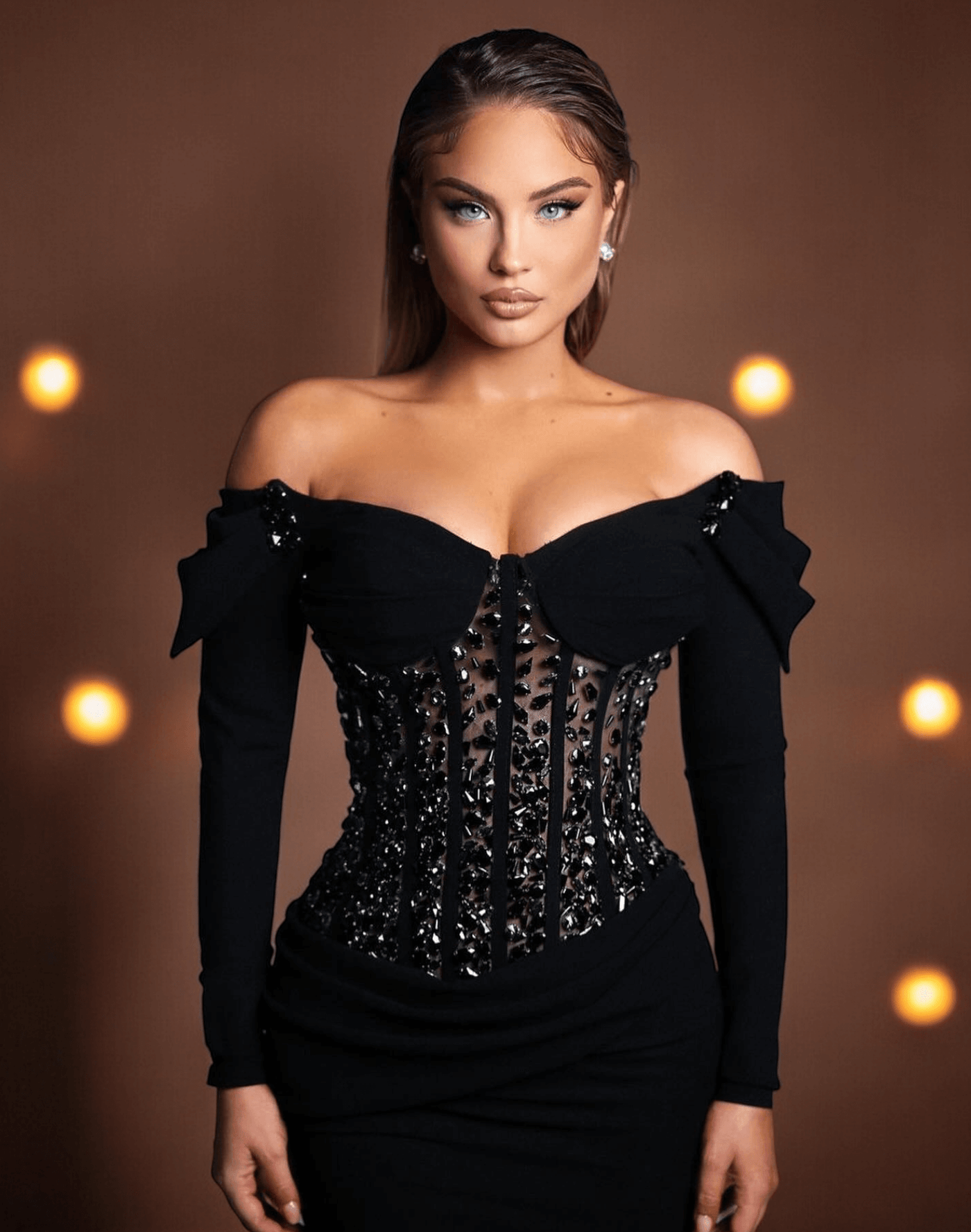 Woman wearing Long Sleeve Crystal Corset Maxi Velvet Dress Black against a brown backdrop with lights